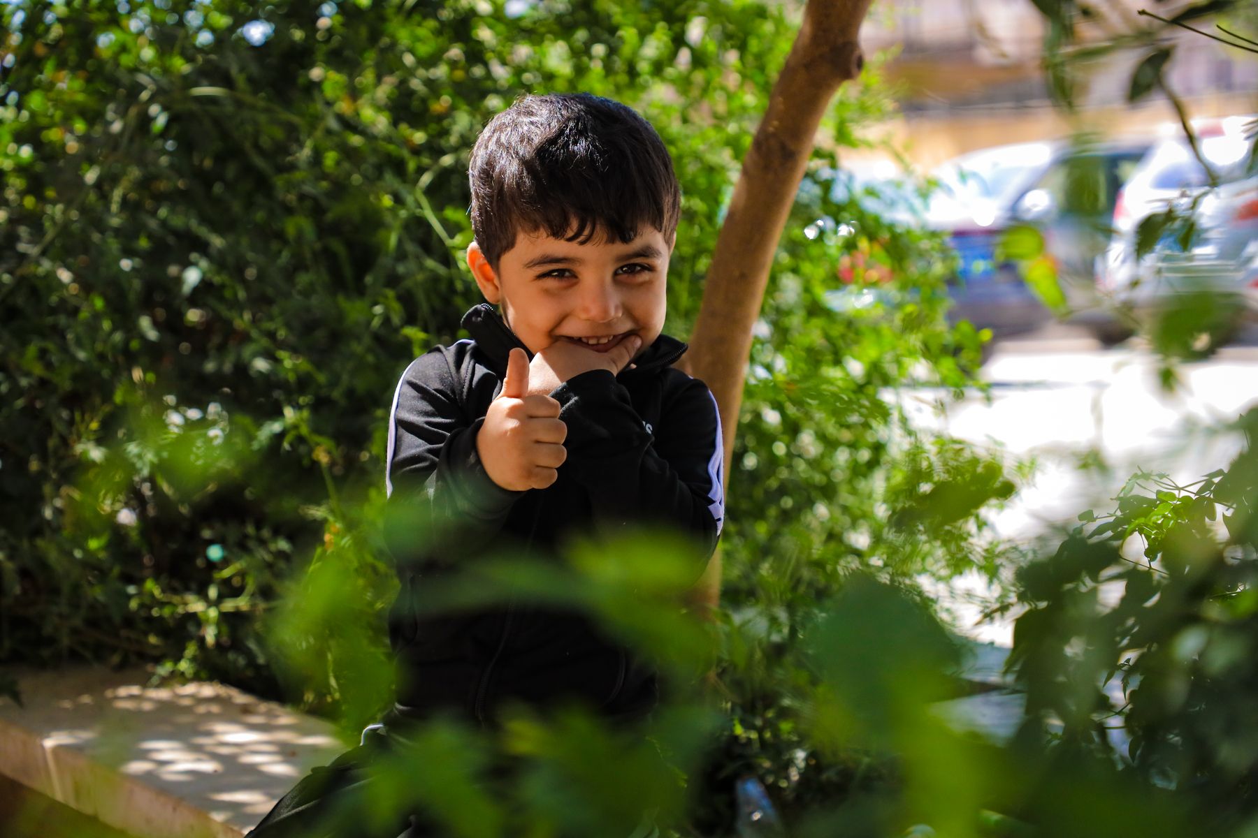 A smiling child outdoors among green leaves